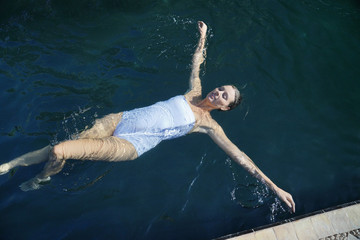 Top view of elegant woman swimming in black tiled pool