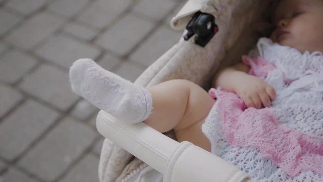Beautiful little girl sleeping in a baby carriage on the street.