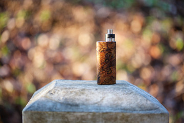 high end natural stabilized wood box mods with rebuildable dripping atomizer on bokeh texture background, vaping device, selective focus