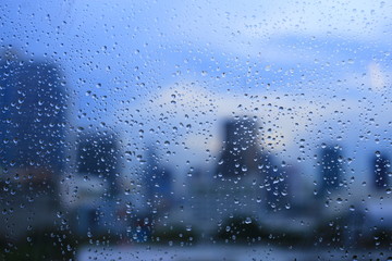 Naklejka na ściany i meble office window covered with rain water. water spray on window. after rain traffic, worker stuck in the office concepts. blur urban skyline background. rainy season concepts.
