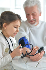 Obraz premium Portrait of granddaughter measuring blood pressure to her grandfather in room