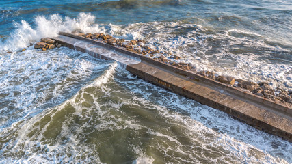 Aerial view on a stone pier against which the force of the sea is raging with high and strong...