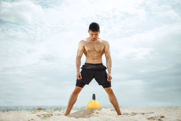 Fototapeta na wymiar Young healthy man athlete doing exercise with the weight at the beach. Signle male model shirtless training at the river side in sunny day. Concept of healthy lifestyle, sport, fitness, bodybuilding.