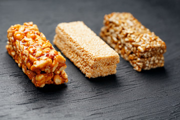 Cereal granola bar with peanuts, sesame and sunflower seeds on a cutting board on a dark stone table. View from above. Three Assorted Bars
