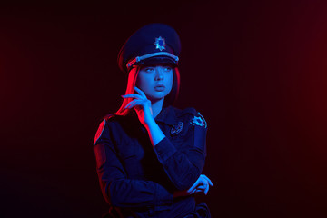 Close-up shot of a redheaded female police officer is posing for the camera against a black...