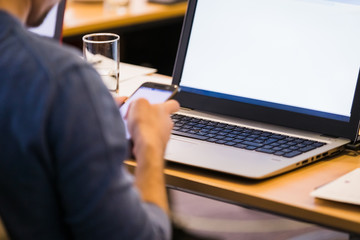 Business person holding smartphone and using blank screen laptop at the office.