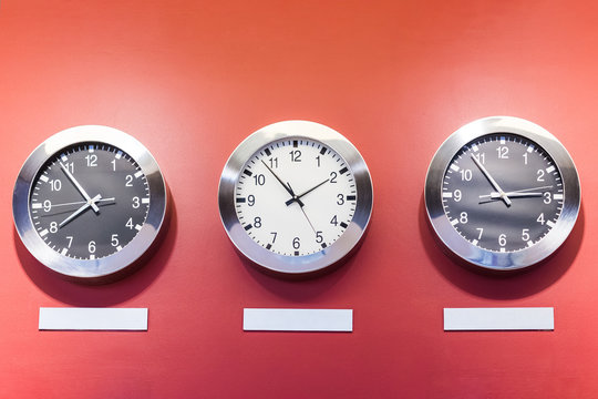 Three clocks on red wall showing different time.