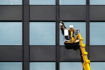 Male window cleaner cleaning glass windows on modern building high in the air on a lift platform....