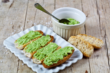 Crostini with avocado guacamole on white plate closeup on rustic wooden table. Diet breakfast.