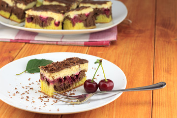 Cocoa cherry cake, called 'Danube Wave'. Top with vanilla cream and chocolate. A plate with a slice of cake at the wooden table.