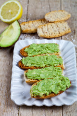 Fresh crostini with avocado guacamole on white plate closeup on rustic wooden table.