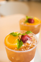 Beverage mocktail orange flavor, mixed with lime and strawberry with ice decorated with mint leaves in a plastic glass.