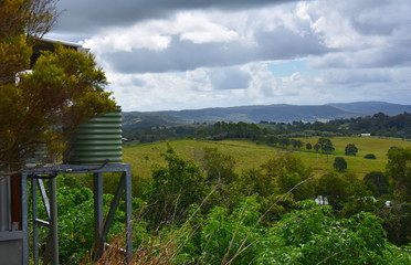 Broad panorama of the countryside on Sunshine Coast Hinterland. Watertank in the foreground, grassy hills in the background. View from Kanyana Park on a cloudy day (Queensland, Australia).