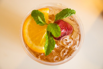 Beverage mocktail orange flavor, mixed with lime and strawberry with ice decorated with mint leaves in a plastic glass.