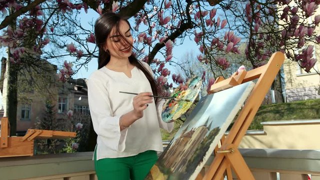 Beautiful girl artist paints his picture on the background of a sakura tree. Near women, easel, bones and paints. Girl pattern ornament art colourful paper fine art color slow motion