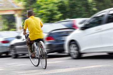 Fototapeta premium Asian men wear yellow shirts, biking with cars running as blurred images in the background. Concept of transportation and Inequality.