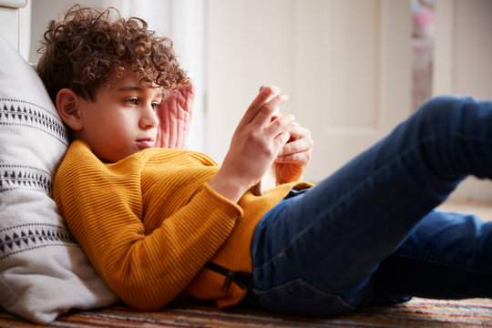 Boy Lying On Floor Of Bedroom Spending Too Much Time Using Mobile Phone