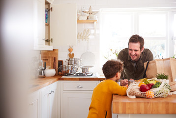 Father And Son Coming Home From Shopping Trip Using Plastic Free Bags Unpacking Groceries In Kitchen