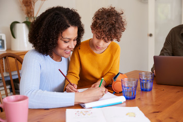 Mother Helping Son With Homework On Kitchen Table At Home