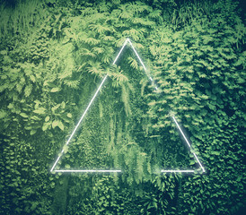 Neon light triangle frame glowing behind tropical green foliage.