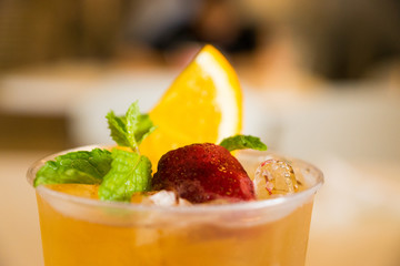 Beverage mocktail orange flavor, mixed with lime and strawberry with ice decorated with mint leaves in a plastic glass.