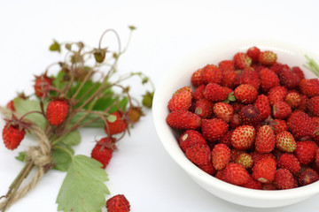 bouquet of wild strawberries close-up on a white background near a plate of berries
