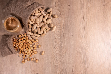 Peanut butter in glass with raw peanuts and poured roasted peanuts, top view photo