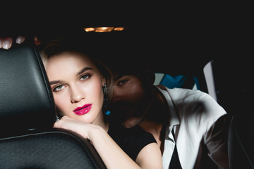 man and young woman sitting in back seat of car in dark and looking at camera