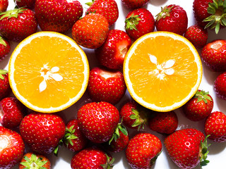 Top view of two orange halves surrounded by red strawberries on white background.