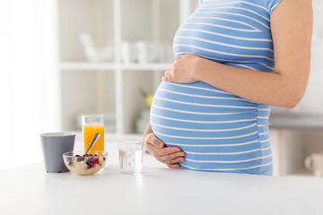 pregnancy, healthy eating and maternity concept - close up of pregnant woman touching her belly with breakfast on kitchen table at home