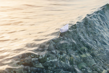 Paper boat sailing on the crest of the waves in the sea