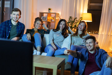 friendship, leisure, people and entertainment concept - happy friends watching tv at home in evening