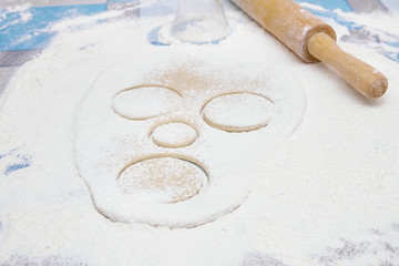 raw dough in shape of face rolled out on a flour covered table