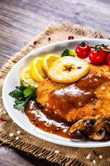 Fried pork chop with vegetables and mushrooms on wooden background