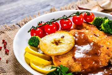 Fried pork chop with vegetables and mushrooms on wooden background