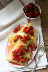 Thin pancakes with cream filling and strawberry sauce on a wooden table. Rustic style.