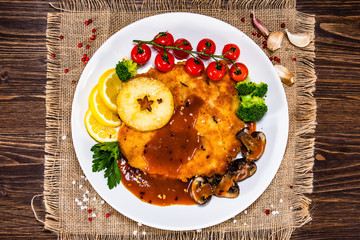 Fried pork chop with vegetables and mushrooms on wooden background