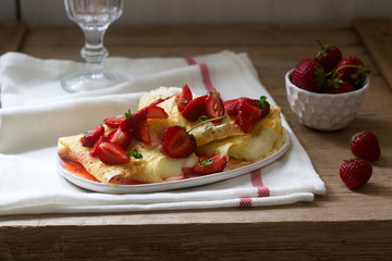 Thin pancakes with cream filling and strawberry sauce on a wooden table. Rustic style.