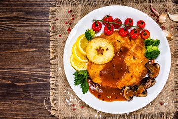 Fried pork chop with vegetables and mushrooms on wooden background