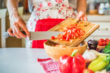 Female hand put chopped bell pepper in wooden bowl in kitchen. Cooking vegetables