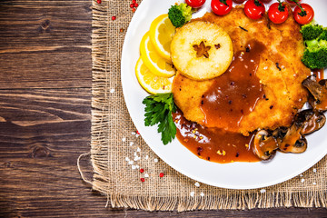Fried pork chop with vegetables and mushrooms on wooden background