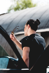 Back view of stylish man with sunglasses posing near car