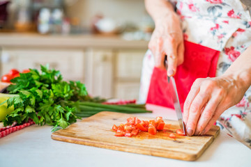 Female hand with knife chops tomato in kitchen. Cooking vegetables