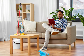 household and people concept - indian man reading book and resting after home cleaning