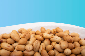 Roasted peanuts in bowl, heap of peanut on blue background, closeup photo