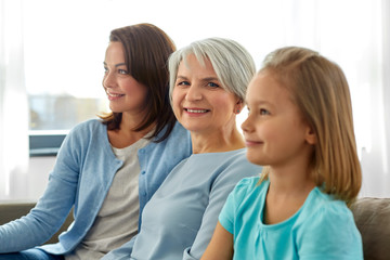 family, generation and female concept - portrait of smiling mother, daughter and grandmother sitting on sofa at home