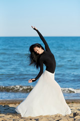 Classical dancer woman. Charming ballerina with windy hair in white chiffon skirt dancing by the sea background. Sun shines on her. Horizontal.