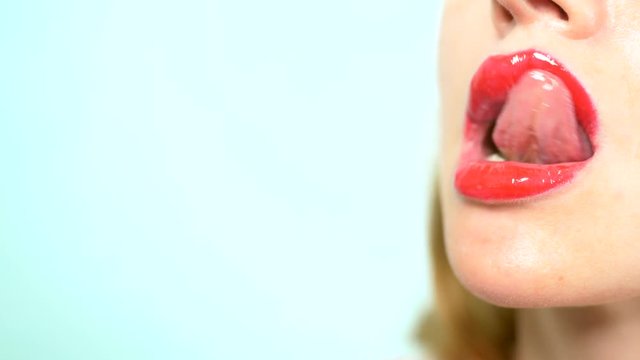 Close-up. sexy lips of a beautiful woman with beautiful red makeup, licks her lips. blows a kiss. copy space. blue background.