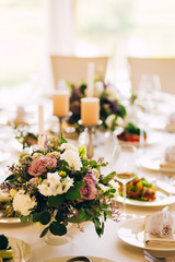 Gorgeous luxury wedding table arrangement, floral centerpiece close up. The table is served with cutlery, crockery and covered with a tablecloth. Wedding party decoration with pink and white flowers.