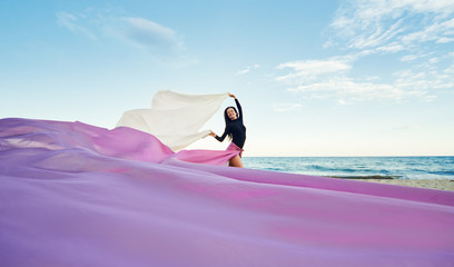 Slim Woman at the beach with long pink fabric. Sky background at the summer. Classic dancer on the...